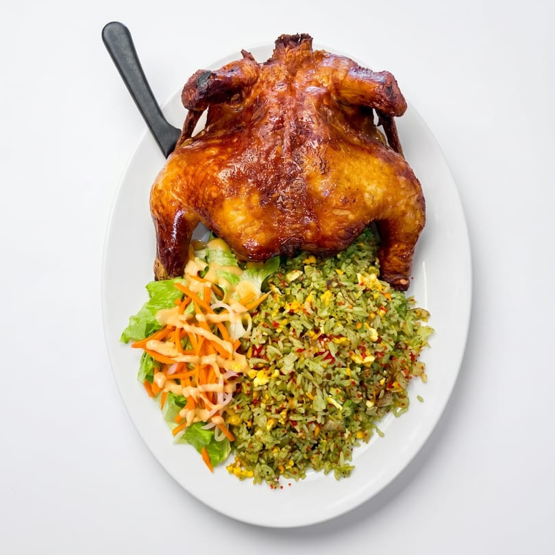 Whole roasted chicken with green rice, salad, and a knife on a white plate.