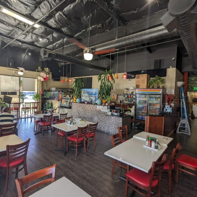 Interior of a restaurant with red chairs, white tables, a mosaic counter, and a beverage cooler.