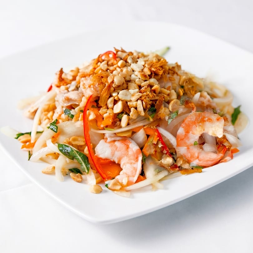 Vietnamese shrimp and chicken salad with peanuts, herbs, and chili on a white plate.