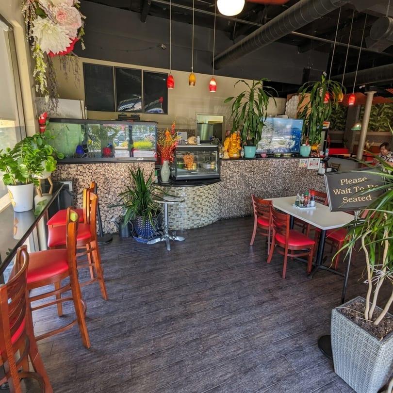 Interior of a restaurant with red chairs, dark wood floors, and a mosaic-tiled counter with plants.